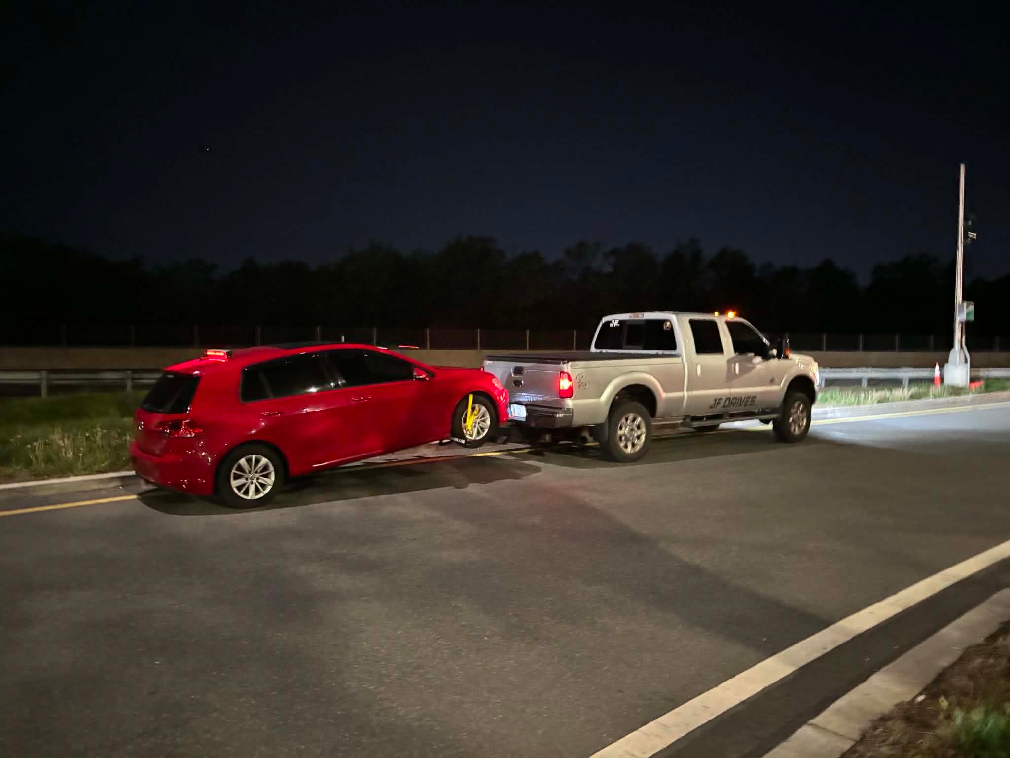 JF Drives towing a red Volkswagen at night